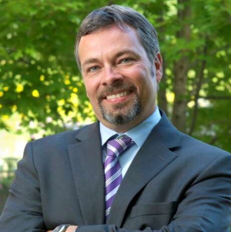 Dr. Bruce McAdams poses for a headshot in front of trees.