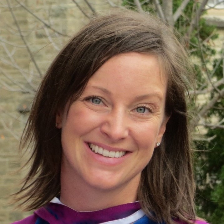 Dr. Katie Lebel poses for a headshot in front of a yellow-brick building and trees