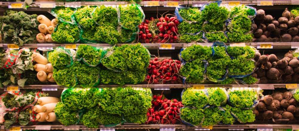 A grocery store shelf filled with various produce including broccoli, squash, lettuce, radishes and beets.