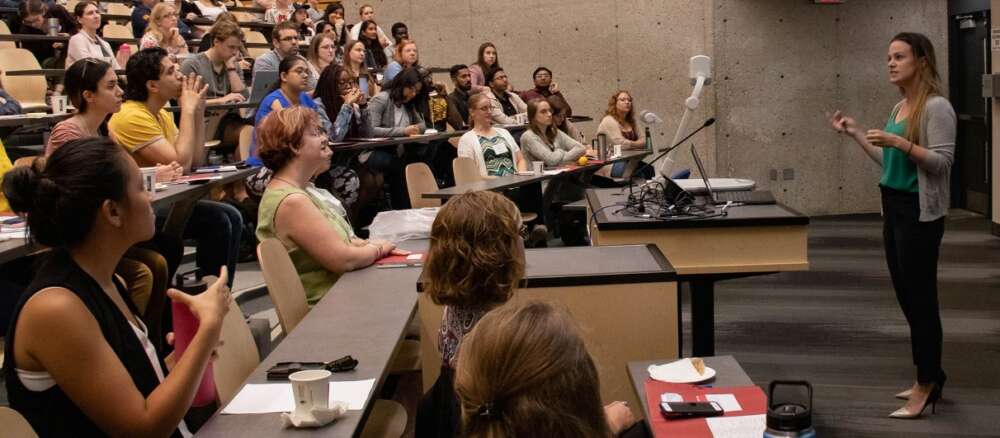 a teacher gestures while standing in front of a large lecture hall