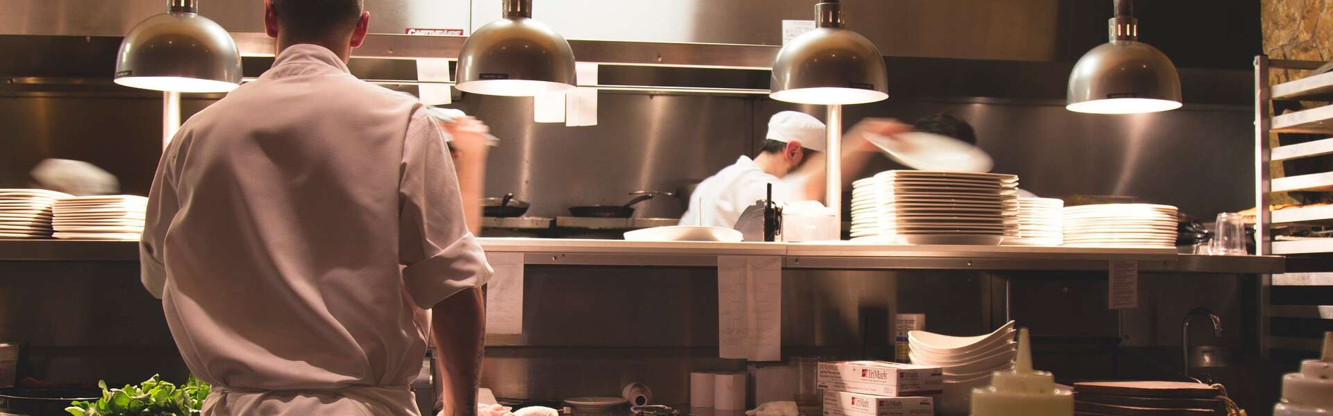 a waiter stands near an open kitchen where chefs work