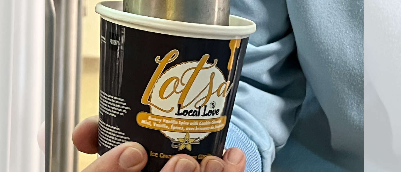 a hand holds a pint container to catch ice cream from a large mixing machine