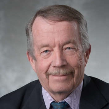 Dr. Ed McBean poses for a photo in front of a cloudy grey backdrop.