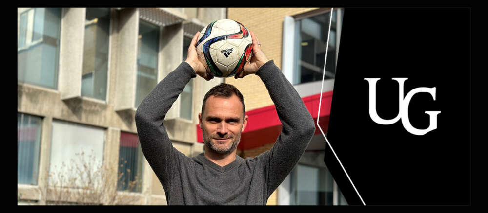 Dr. Alan McDougall holds a soccer ball over his head and smiles for the camera