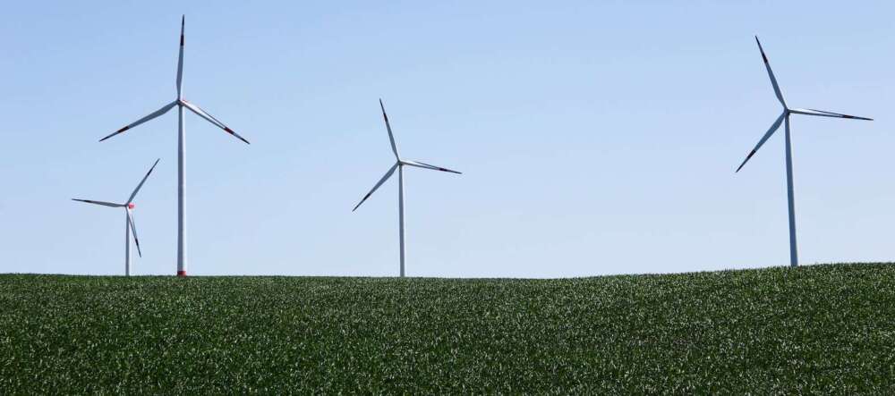 Four wind turbines in a green field against a blue sky.