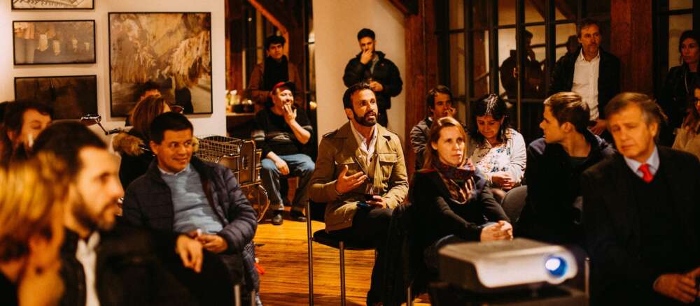 An audience member speaks as people sit in chairs watchinga slide presentation in an art gallery-like setting