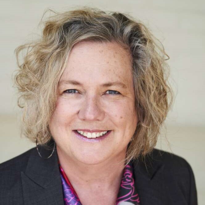 Head and shoulders photo of Dr. Samantha Brennan. She is wearing a black blazer and a purple and red scarf. She is standing in front of a white wall.