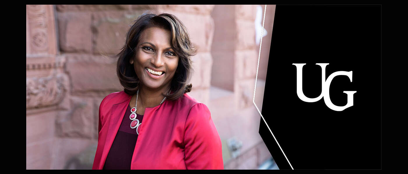 Indira Naidoo-Harris stnads against a sandstone building and smiles for the camera