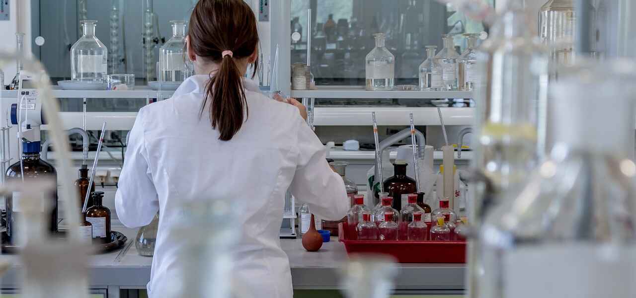 A woman wearing a white lab coat and her hair in a ponytail, works in a science lab