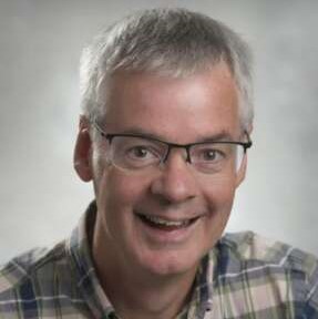 Doug Goff smiles for a photo in front of a grey backdrop