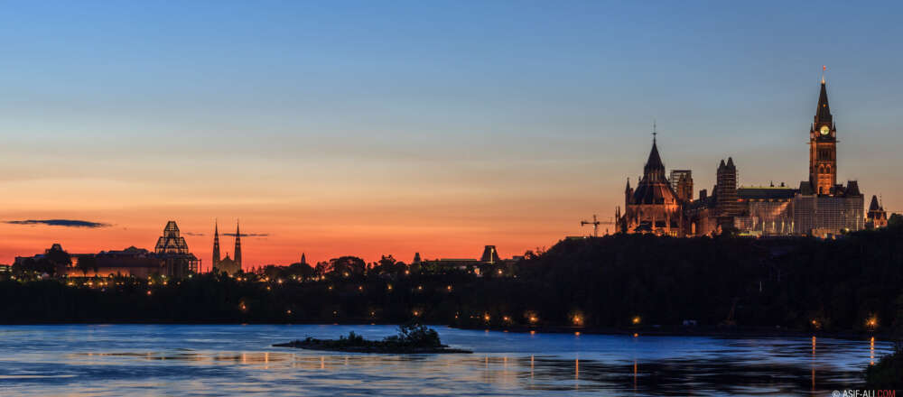 Parliament Hill and the Ottawa skyline are silhouetted at sunrise behind the Rideau River