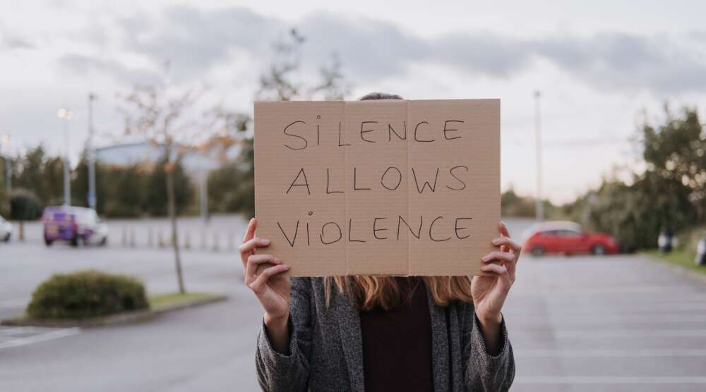Unrecognizable woman in casual clothes standing on road and demonstrating poster Silence Allows Violence
