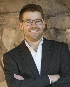 Dr. Gus Skorburg poses for a photo in front of a stone wall