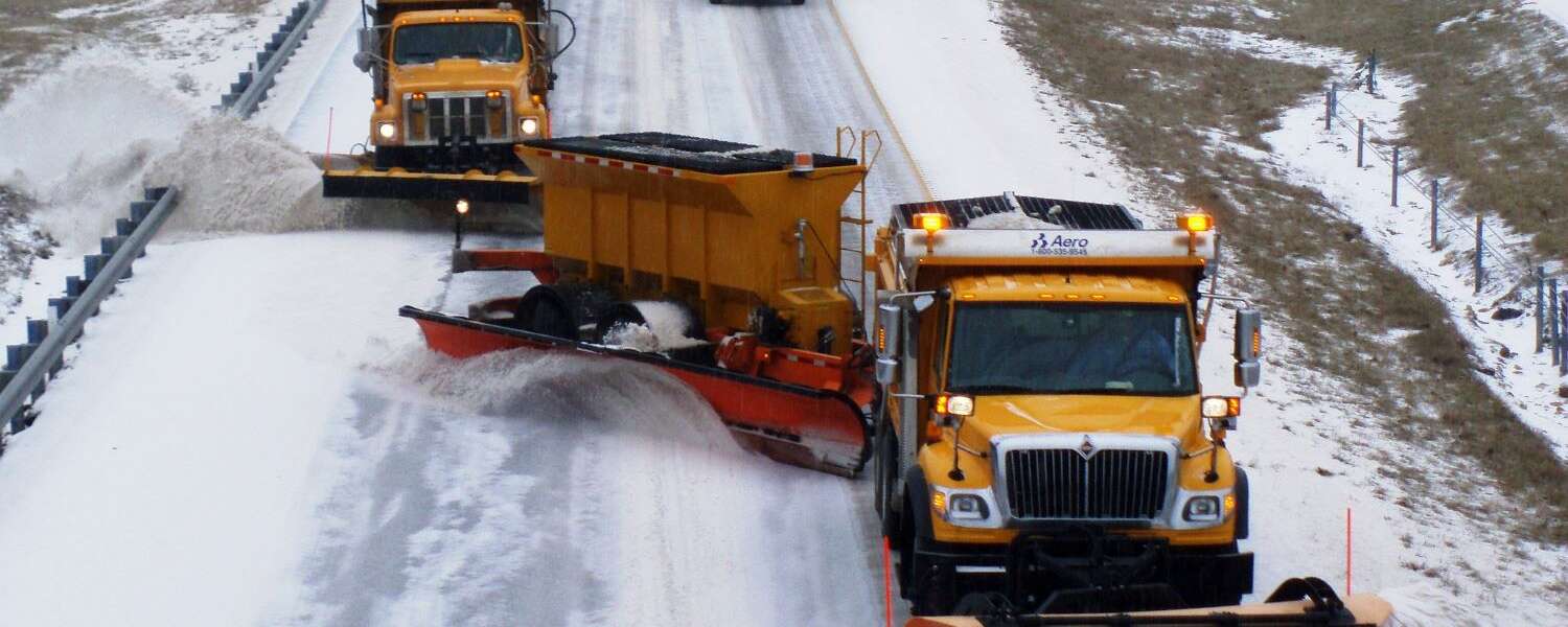 Three yellow snow plows lead traffic on a snowy road
