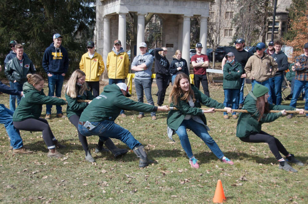 Participants pull on a rope during a tug-a-war competition outdoors while onlookers watch from behind