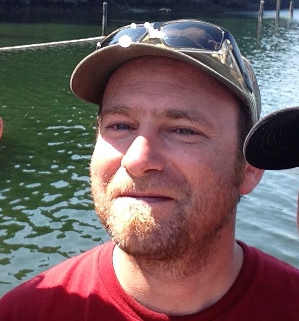 a person in a ballcap stands on a dock in front of a lake