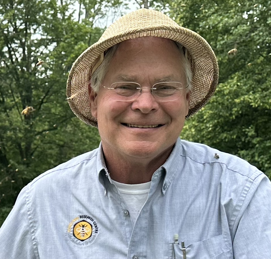 A closeup of a smiling Paul Kelly wearing a hat and a dress shirt with the HBRC logo