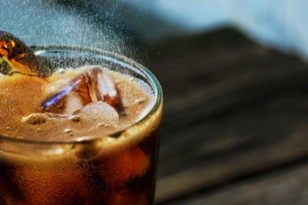 A black carbonated beverage fizzes in a glass upon a pile of ice cubes.