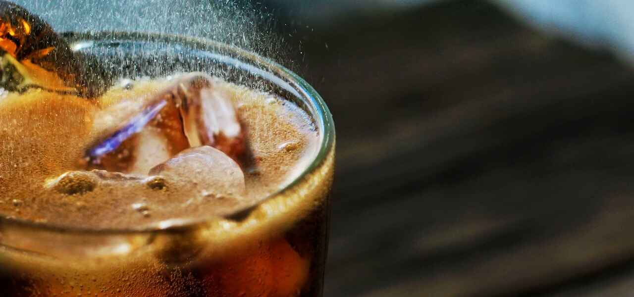 A black carbonated beverage fizzes in a glass upon a pile of ice cubes.