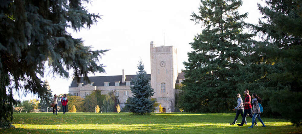 Three people walk across the lawn of Johnston Green on sunny day