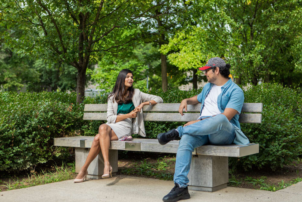 A man and a woman sitting on a park bench, talking.