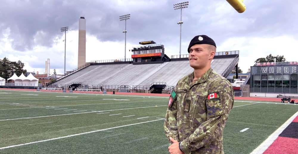 a reservist soldier wears an operational uniform while standing on a football field with bleachers behind