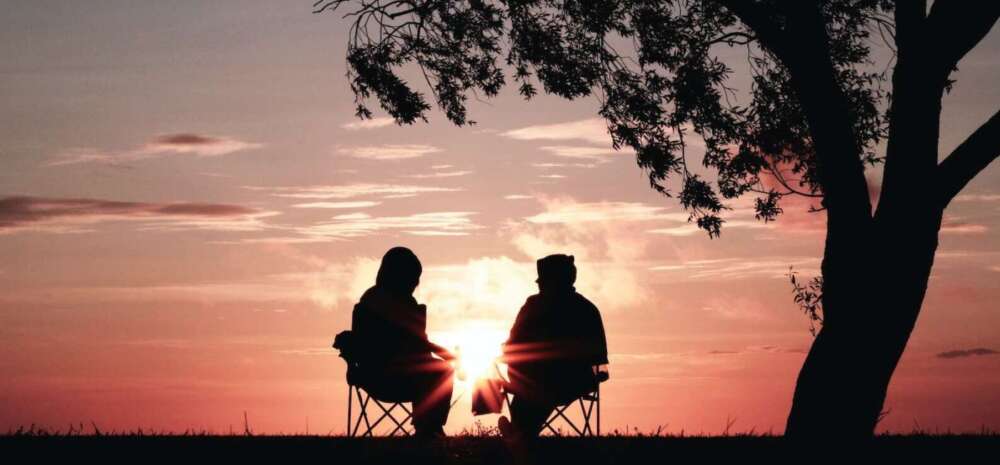 silhouette of two person sitting on chair near tree