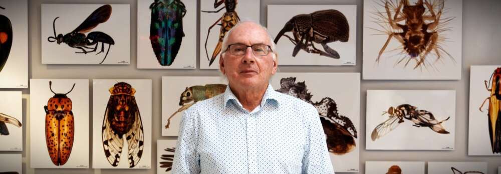Dr. Paul Hebert poses for a portrait in the atrium of the Centre for Biodiversity Genomics at the University of Guelph with canvas prints of magnified photos of insects hanging on the wall behind him