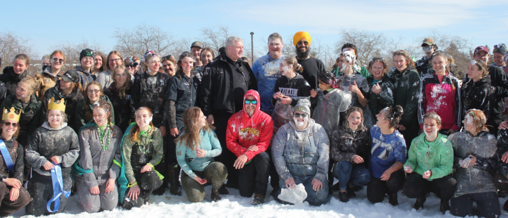 Group of about 35 students smiling on a winter field, some wearing crown and ribbon