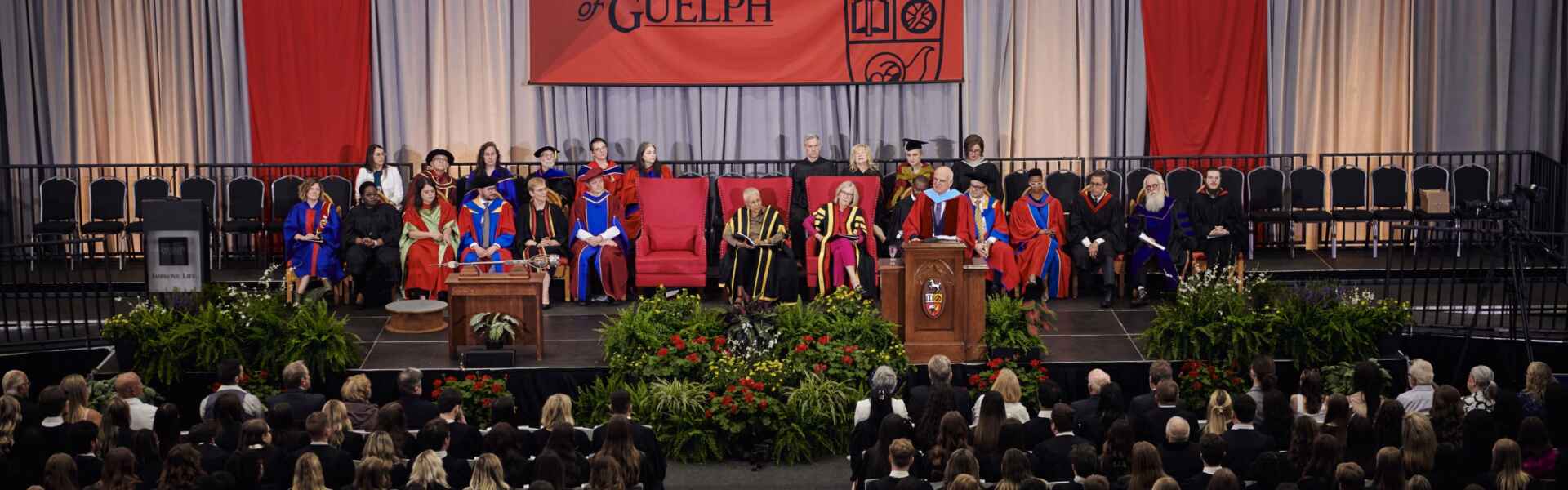 A wide shot of a convocation ceremony with several people in regalia sitting on stage facing out to a large audience