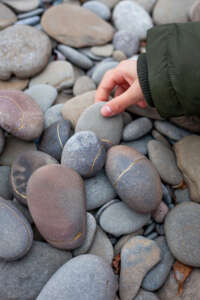 A person's hand picks up a smooth stone from a pile of stones.