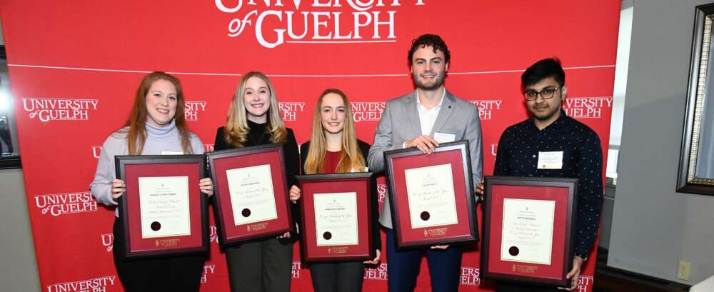 Five people holding framed award pose for a photo in front of a University of Guelph banner