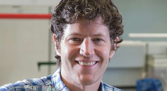 Headshot of David McCarthy, smiling and wearing a button up plaid shirt.