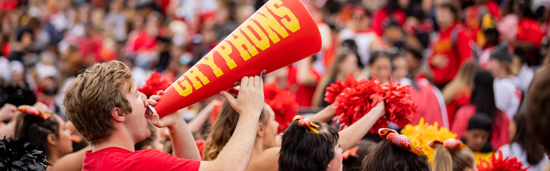 fans dressed in red cheer in the stands, one man holds a red megaphone that says gryphons