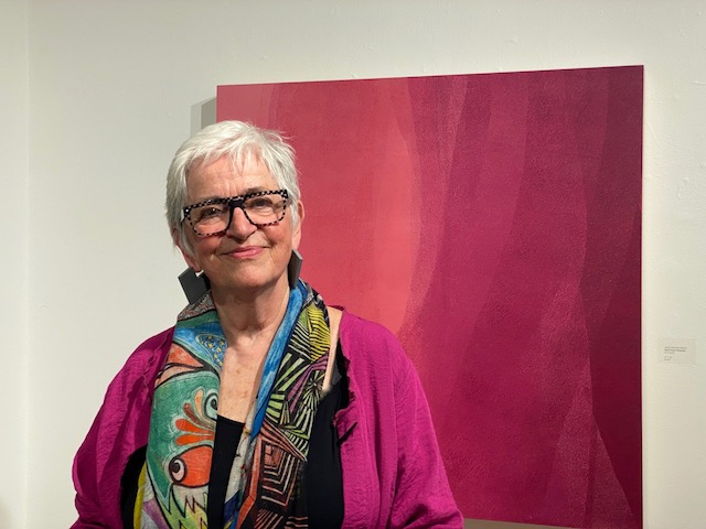 Headshot of Janice Mason Steeves, standing in front of one of her paintings.