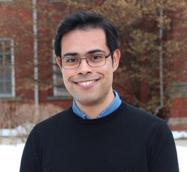 a man in a dark sweater with a light blue collar poses for a headshot