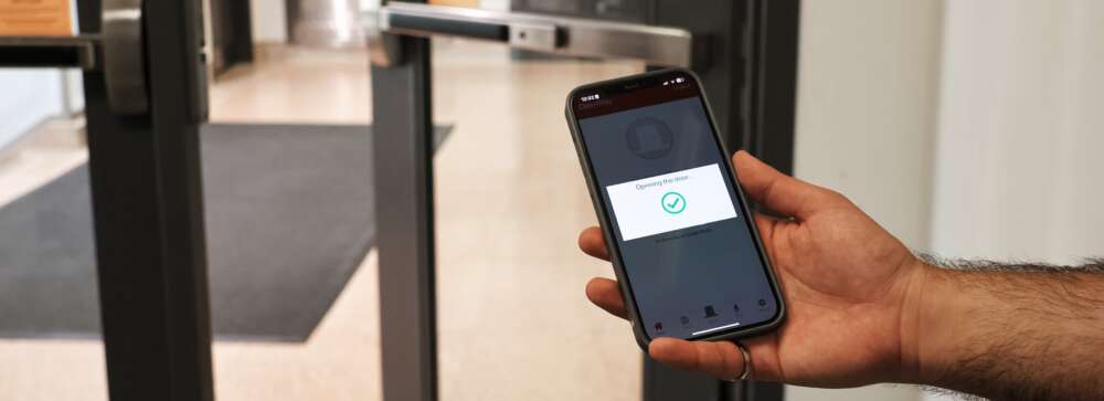 a hand holds a cell phone while a door opens in the background