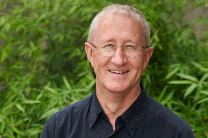 Wayne Caldwell headshot - he stands in front of a green plant.