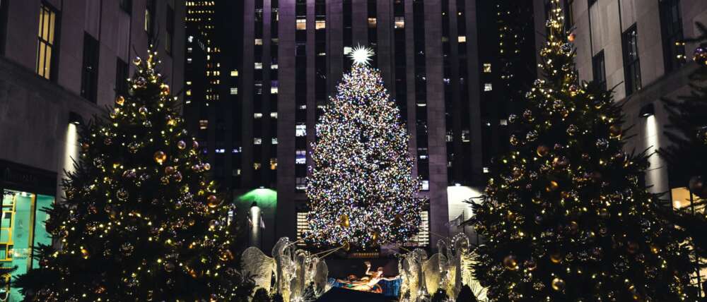 Three christmas trees light up urban street, a nativity scene is in the foreground