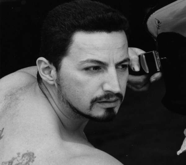 Black and white photo of the head and shoulders of a shirtless man staring off to the side an holding some kind of object.