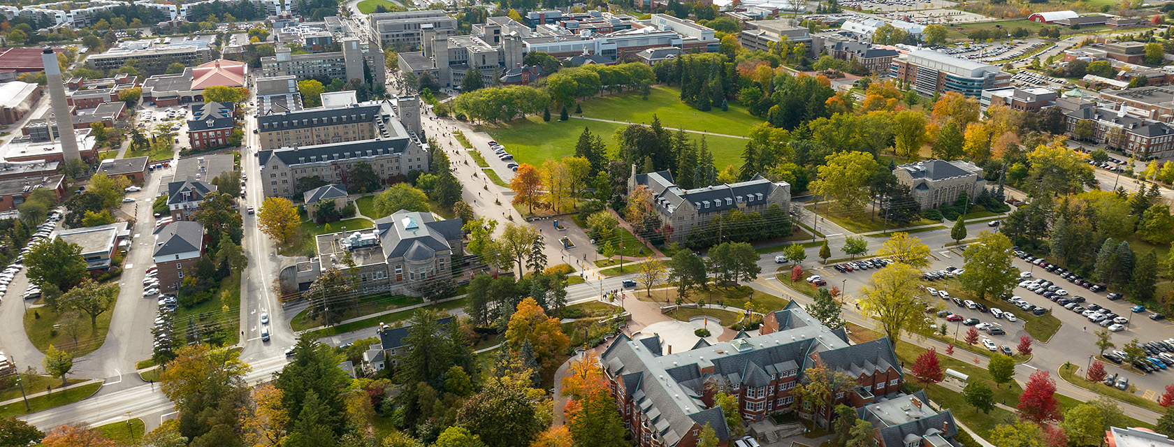 An aerial view of the University of Guelph campus depicts multiple buildings among lush trees and Johnston Green.