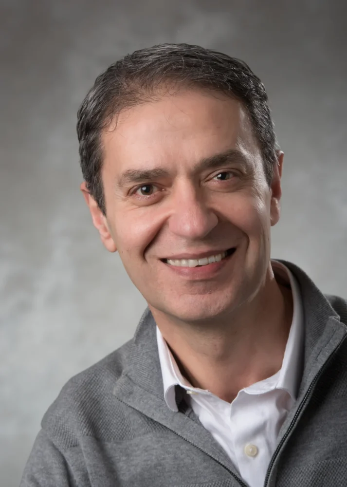 a man in a grey jacket and white shirt poses for a headshot