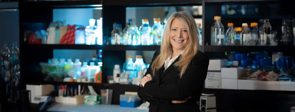 a woman in a black blazer and white shirt with blonde hair poses for a headshot in a lab