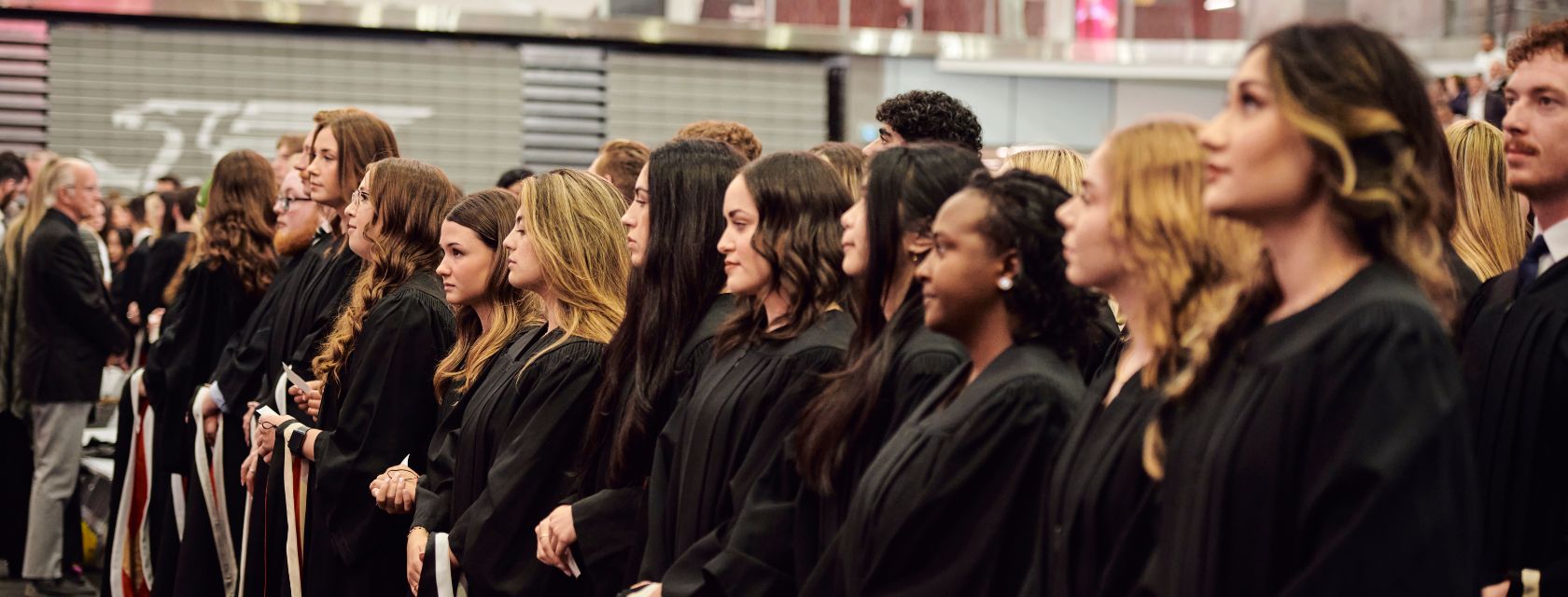 a group of students in black grad gowns wait for a convocation ceremony