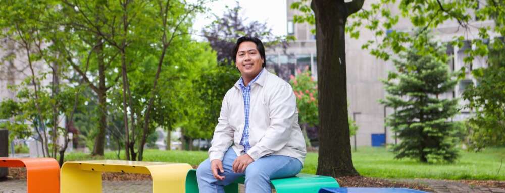 A person sits on one of 4 coloured benches that form a rainbow on the University of Guelph campus