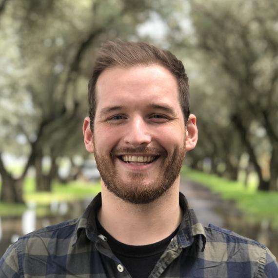 A person with brown hair wearing a plaid shirt poses for a headshot