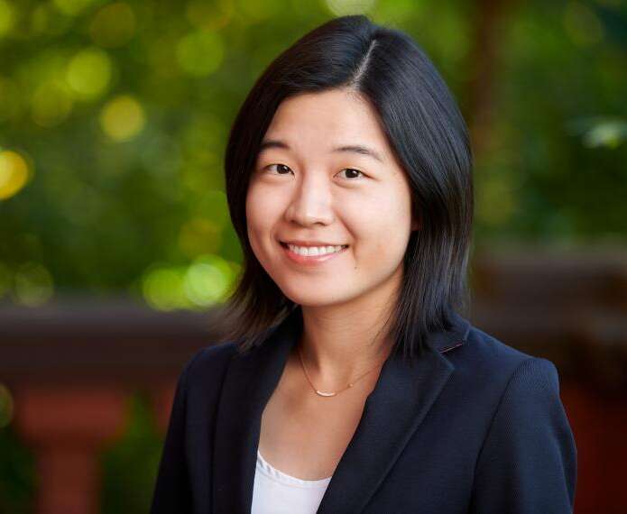 a person with black in a white shirt and navy blazer poses for a headshot in front of a green background