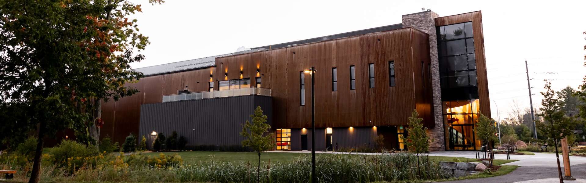 A wooden building sits illuminated at dusk surrounded by landscaping and trees.