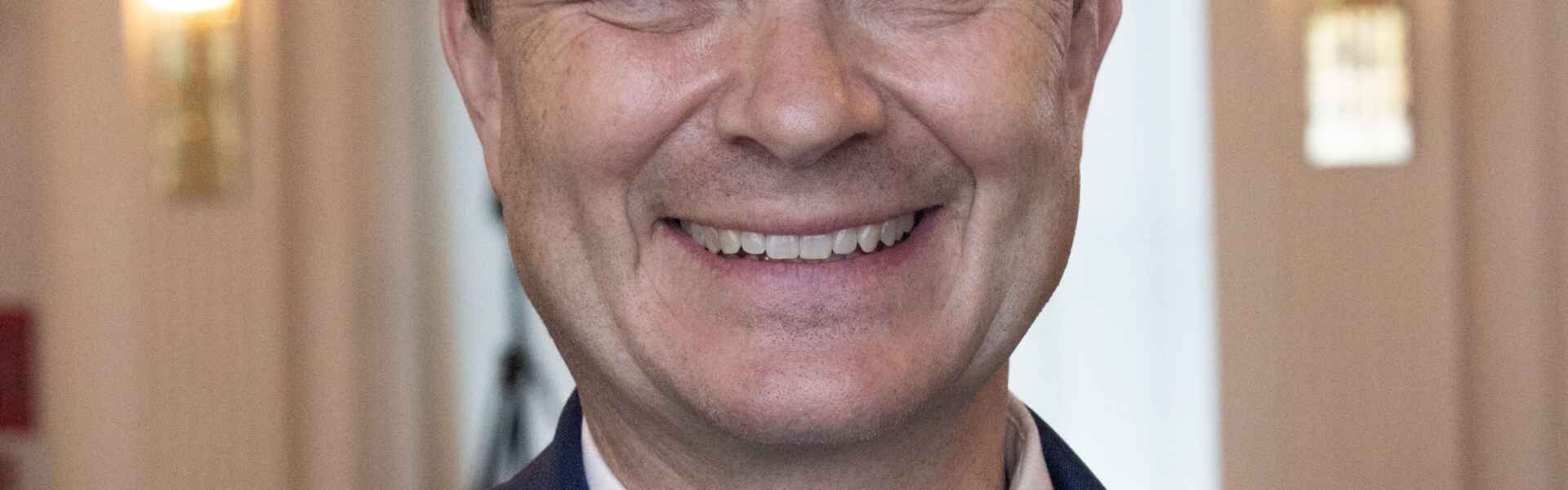 a person with short hair wearing a navy blue jacket and blue vest poses for a headshot