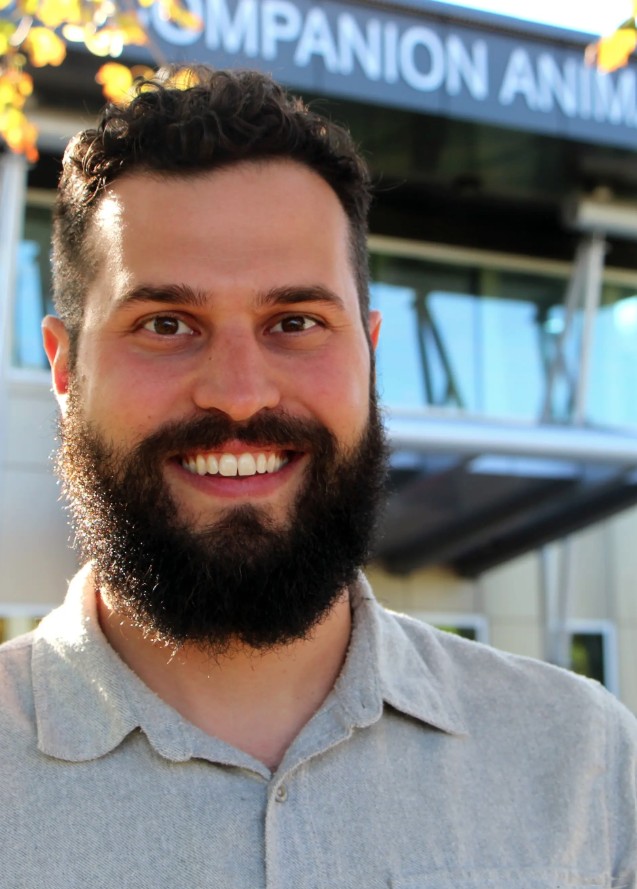 a person with brown hair and facial hair wearing a grey collared shirt poses for a headshot